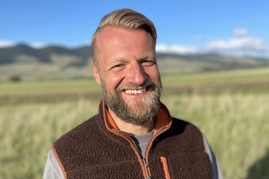 middle aged man in grey shirt and brown sleeveless sweater smiling on field